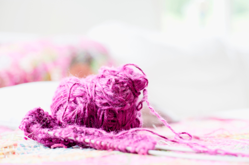 Fotografi av et garnnøste. Foran nøstet ligger et strikketøy med strikkepinner.