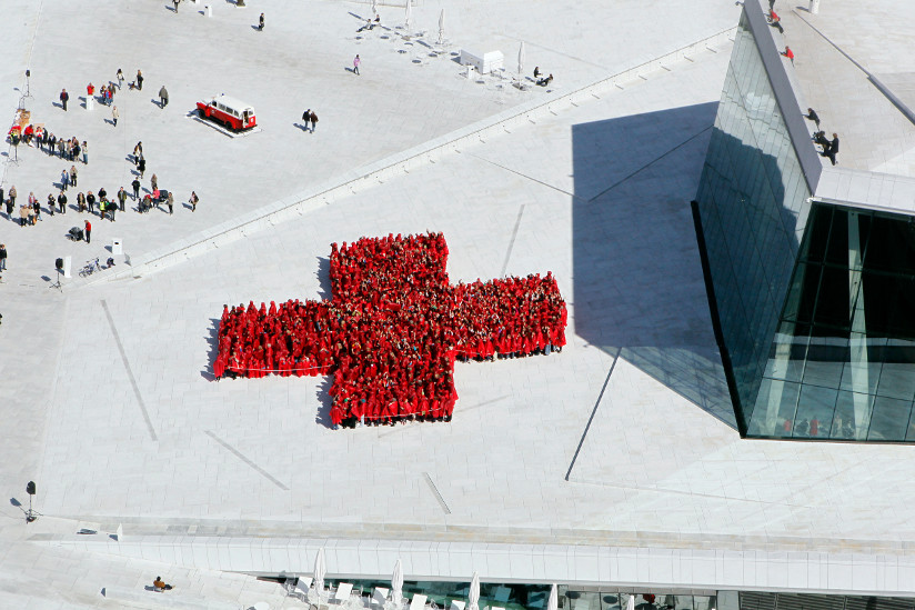 Fotografi av rødkledde personer som danner et menneskelige kors på taket av operahuset i Oslo.