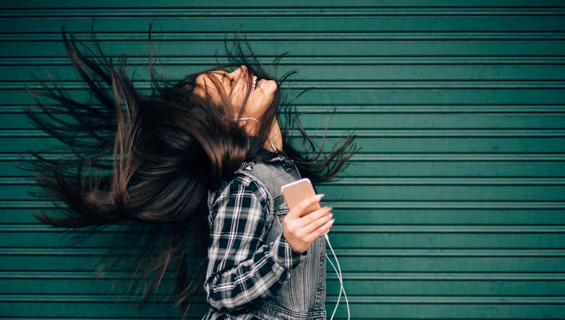 Fotografi av en jente som lytter og danser til musikk hun lytter til via smarttelefon.