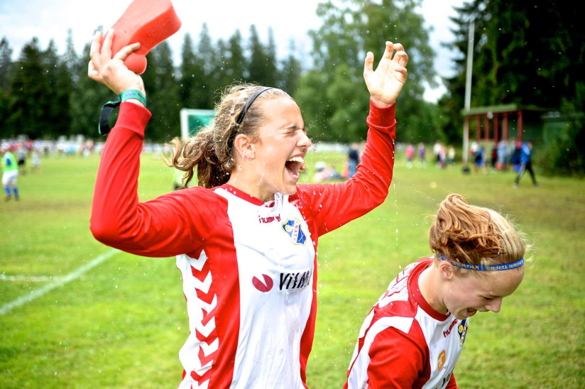 Fotografi av to jenter som nettopp har spilt fotballkamp. Draktene de har på seg viser logoene til bedriftene som sponser fotballaget.