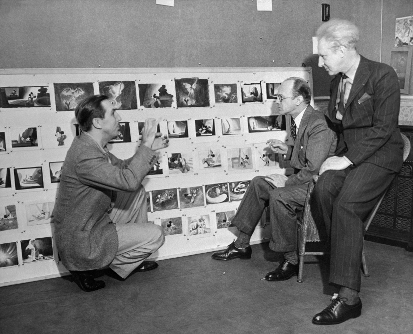 Svart-hvitt fotografi av Walt Disney som diskuterer musikken til Fantasia – en 2 og en halv times symfoni med animasjoner – med komponistene Deems Taylor og Leopold Stokowskiav.