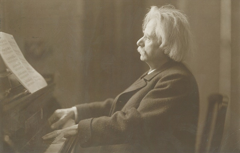 Svart-hvitt fotografi av Edvard Grieg som spiller på et flygel, ca 1900.