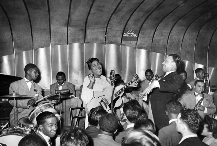 Svart-hvitt fotografi av Sister Rosetta Tharpe (1915-1973) som framfører blues på en scene sammen med band.