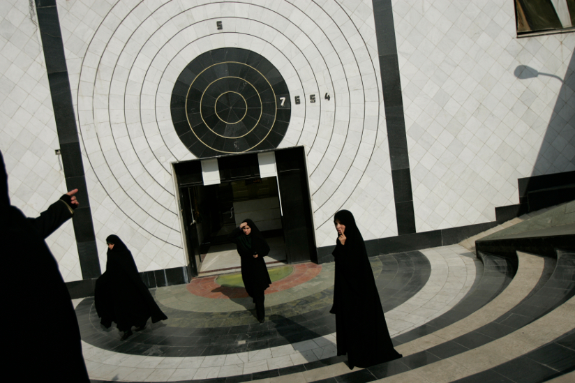 Fotografi av fire kvinner med hijab foran et inngangsparti. En kvinne, som er delvis synlig i forgrunnen, peker mot veggdekorasjonen over inngangen som er en skyteskive.