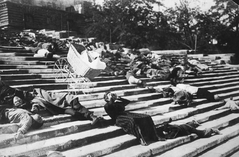 Svart-hvitt fotografi hentet fra den russiske stumfilmen Panserkrysseren Potemkin fra 1925. Fotografiet viser døde mennesker som ligger på trappene ved havnen i Odessa. Midt i stillbilde ser vi en barnevogn som er på vei ned trappene. I forgrunnen ser vi en skadet mann som fører hendende opp mot hodet.